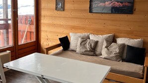 Une pièce chaleureuse avec un mur en bois, un canapé avec des coussins, une table blanche et un tableau représentant des montagnes.