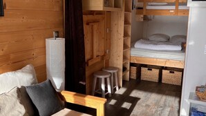 Une pièce de taille modeste, avec un canapé en bois, un lit superposé et des étagères intégrées en bois.