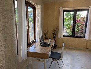 Une petite pièce bien rangée, avec une table en bois, un ordinateur portable, une chaise blanche et deux plantes en pot.