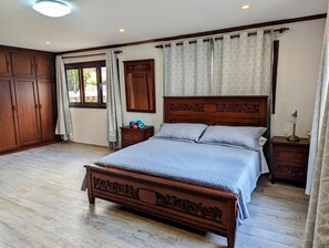 Une chambre à coucher avec un grand lit en bois, une table de chevet, une armoire et une fenêtre avec des rideaux.