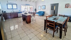 A spacious kitchen with a large island, a dining area with wooden furniture, and a living space with a blue sofa and a beach-themed wall decoration.