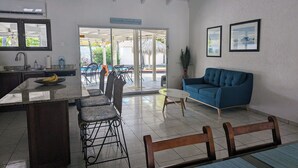 A spacious living area with a blue sofa, a dining table with chairs, a kitchen area with a counter, and a sign reading "Seaside Sanctuary".