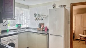Keittiössä on pesukone, jääkaappi, pesuallas ja ikkuna, jossa on verhot.