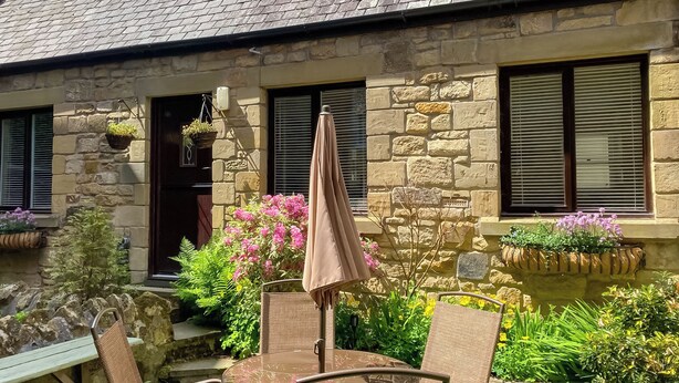 A stone building with a sloped roof, two skylights, and a small patio with a table and chairs. - 2 bedroom accommodation in Alnwick (Alnwick)