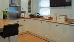 A modern kitchen with white cabinetry, a wooden countertop, a black chair, and a flat-screen TV mounted on the wall. - 2 bedroom accommodation in Alnwick (Alnwick)