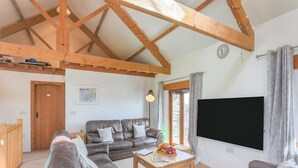 Ein Wohnzimmer mit Holzboden, einer Sofagarnitur, einem Couchtisch mit Obst und einem Fernseher.