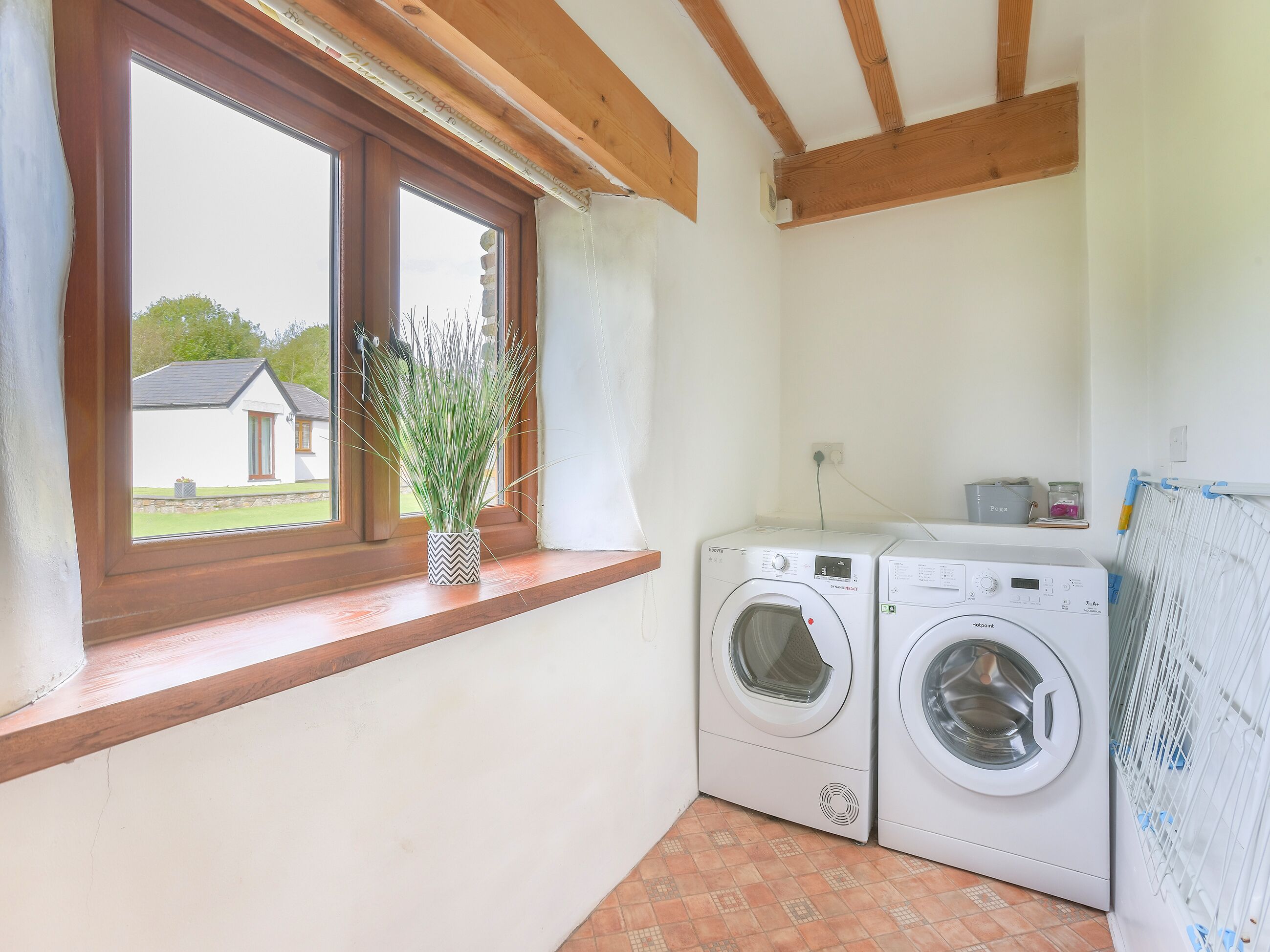 Une buanderie équipée de deux machines à laver, une fenêtre donnant sur une maison et une plante en pot posée sur le rebord de la fenêtre.