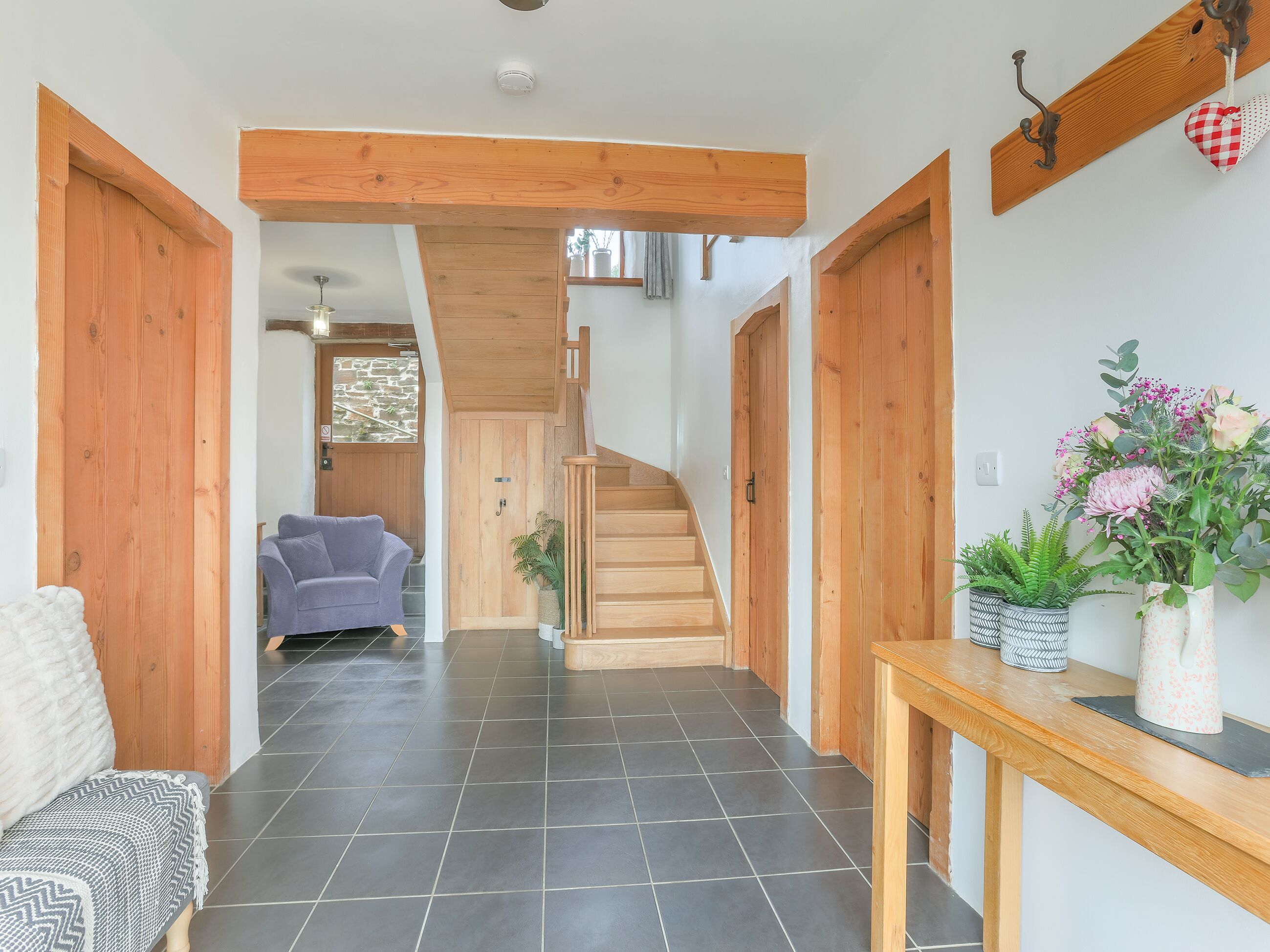A hallway with a wooden staircase, a sofa, a table with plants, and a door.