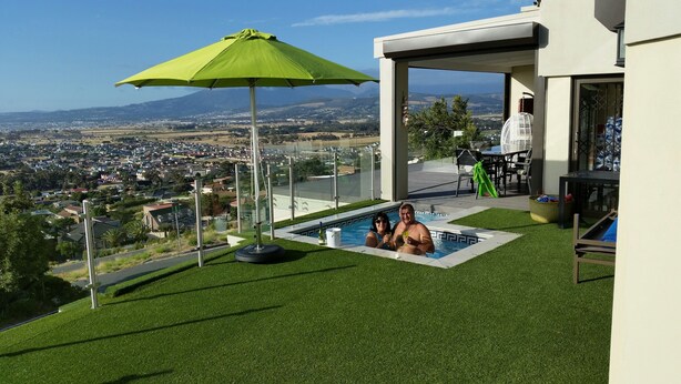A swimming pool with a view of a cityscape, a green umbrella, and a glass-enclosed patio area. - Private Villa With Magnificent Sea Views  (Cape Town)