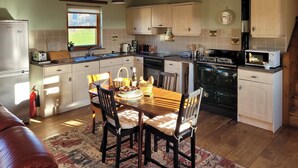 Una cocina con armarios de madera, una mesa de comedor con sillas, un refrigerador, una estufa y un microondas.