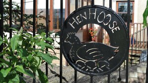 Un letrero de metal con la palabra 'Henhouse' y un diseño de gallina, sujeto a una cerca rodeada de follaje.