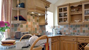 A kitchen with wooden cabinets, a tiled backsplash, a dining table with chairs, a toaster, a kettle, and a vase with flowers. - 3 bedroom accommodation in Llanbedrgoch, near Benllech (Llanbedrgoch, near Benllech)
