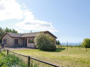 Uma casa de pedra com telhado de telhas, um quintal cercado e vista para o mar.