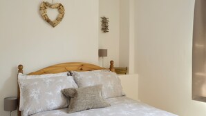 Una cama bien hecha con cabecera de madera, una lámpara de noche y una mesita de noche de madera con un libro.