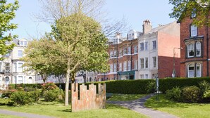 Una calle residencial con casas adosadas, un camino bordeado de árboles y un seto.