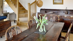Een houten eettafel met stoelen, een vaas met bloemen, een houten bank, een trap en een wandlamp.
