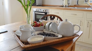 Een ontbijtsetting met een dienblad vol eten, waaronder aardbeien, bosbessen en yoghurt, in een keuken met witte kasten en een houten aanrecht.