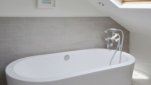 Een moderne badkamer met een vrijstaand bad, grijze betegelde wanden en een dakraam erboven.