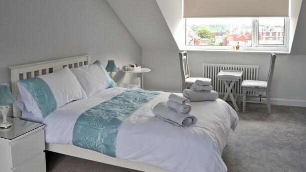 Een slaapkamer met een bed, nachtkastje, lamp, stoel en een raam met uitzicht.