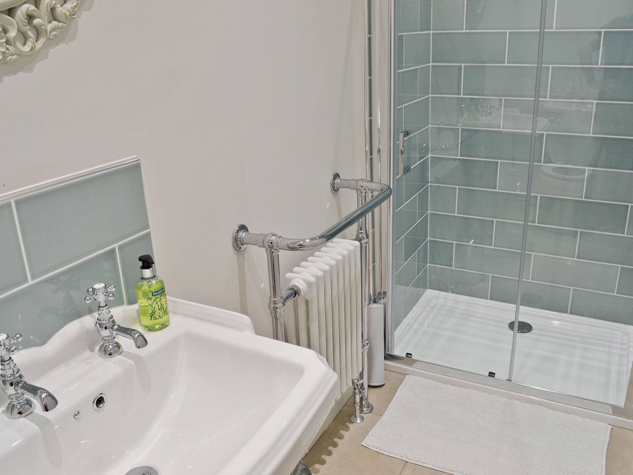 A bathroom with a white sink, a glass shower enclosure, and a white bath mat.