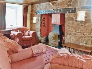 A cozy room with a stone fireplace, a red armchair, and a sofa. - 5 bedroom accommodation in Llanfaethlu, Anglesey (Llanfaethlu, Anglesey)