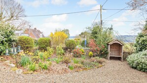 Ein Garten mit Kiesweg, verschiedenen Pflanzen, einer Holzkonstruktion und einem Haus im Hintergrund.