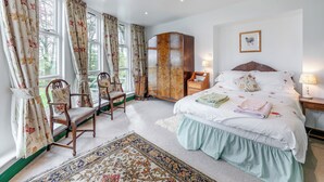 Ein Schlafzimmer mit einem großen Bett, zwei Stühlen, einem Holzschrank und einem Nachttisch mit einer Lampe.