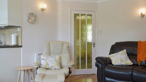 Un salon comprenant un fauteuil beige, un canapé en cuir noir, une petite table d’appoint en bois et une porte blanche dotée de panneaux en verre dépoli.