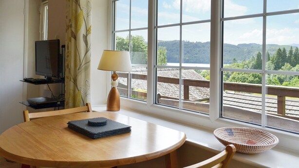 Une pièce avec une grande fenêtre, une table avec une lampe, un téléviseur et une chaise.