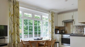 Une cuisine avec des meubles blancs, une cuisinière et un évier. On y trouve une table à manger avec des chaises et un téléviseur posé sur un meuble.