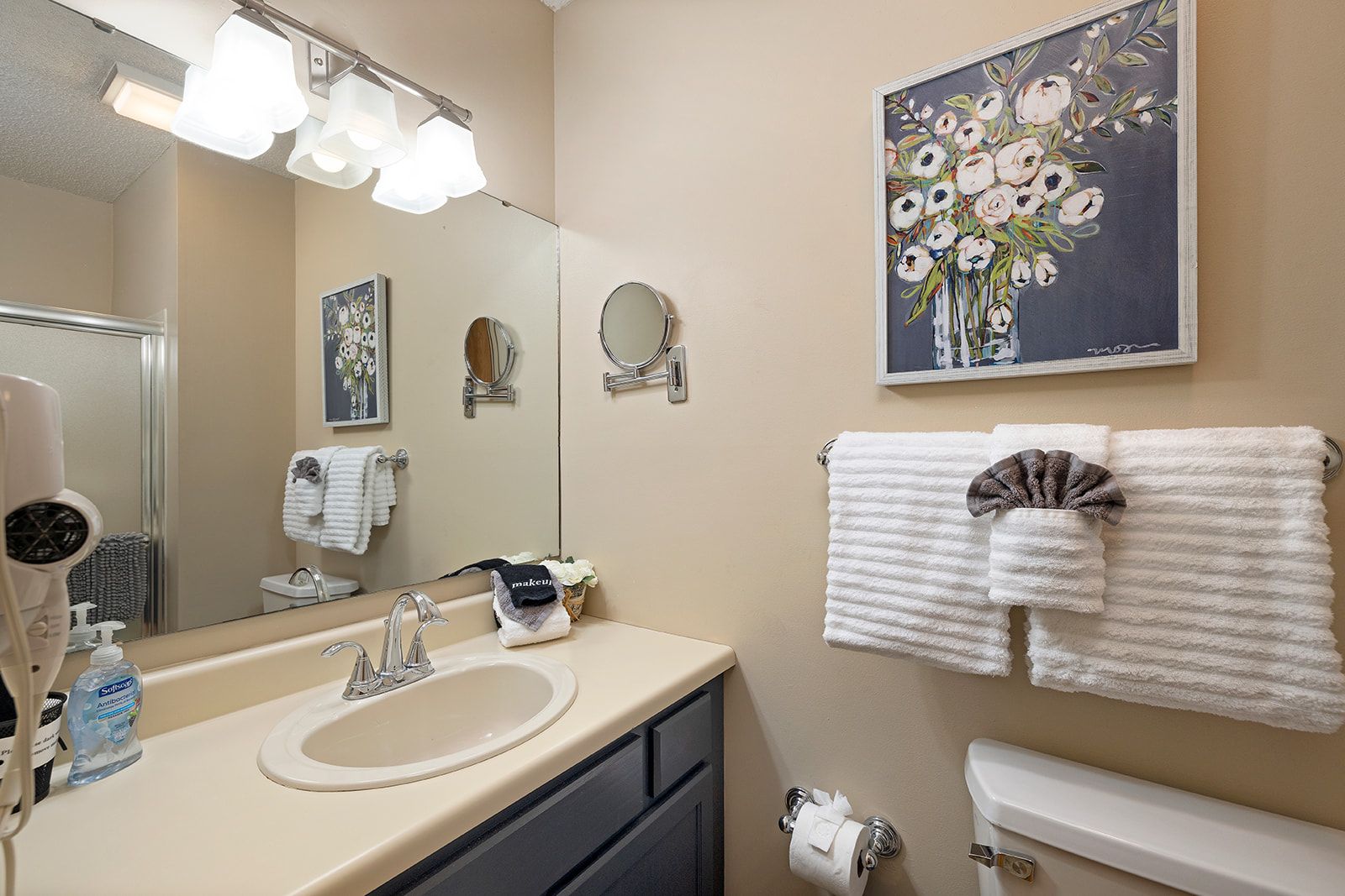 A bathroom with a sink, mirror, towel rack, and a painting of flowers.