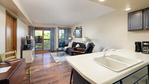 A modern kitchen with a white countertop and sink, a dining area with a wooden table and chairs, and a living area with a sofa and a TV. - Guests say amazing views, 2 miles to SDC (Reeds)