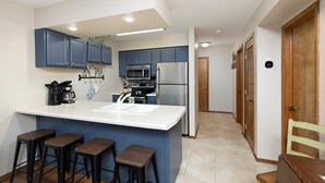 A modern kitchen with blue cabinets, a large island with stools, stainless steel appliances, and a white countertop. - Guests say amazing views, 2 miles to SDC (Reeds)