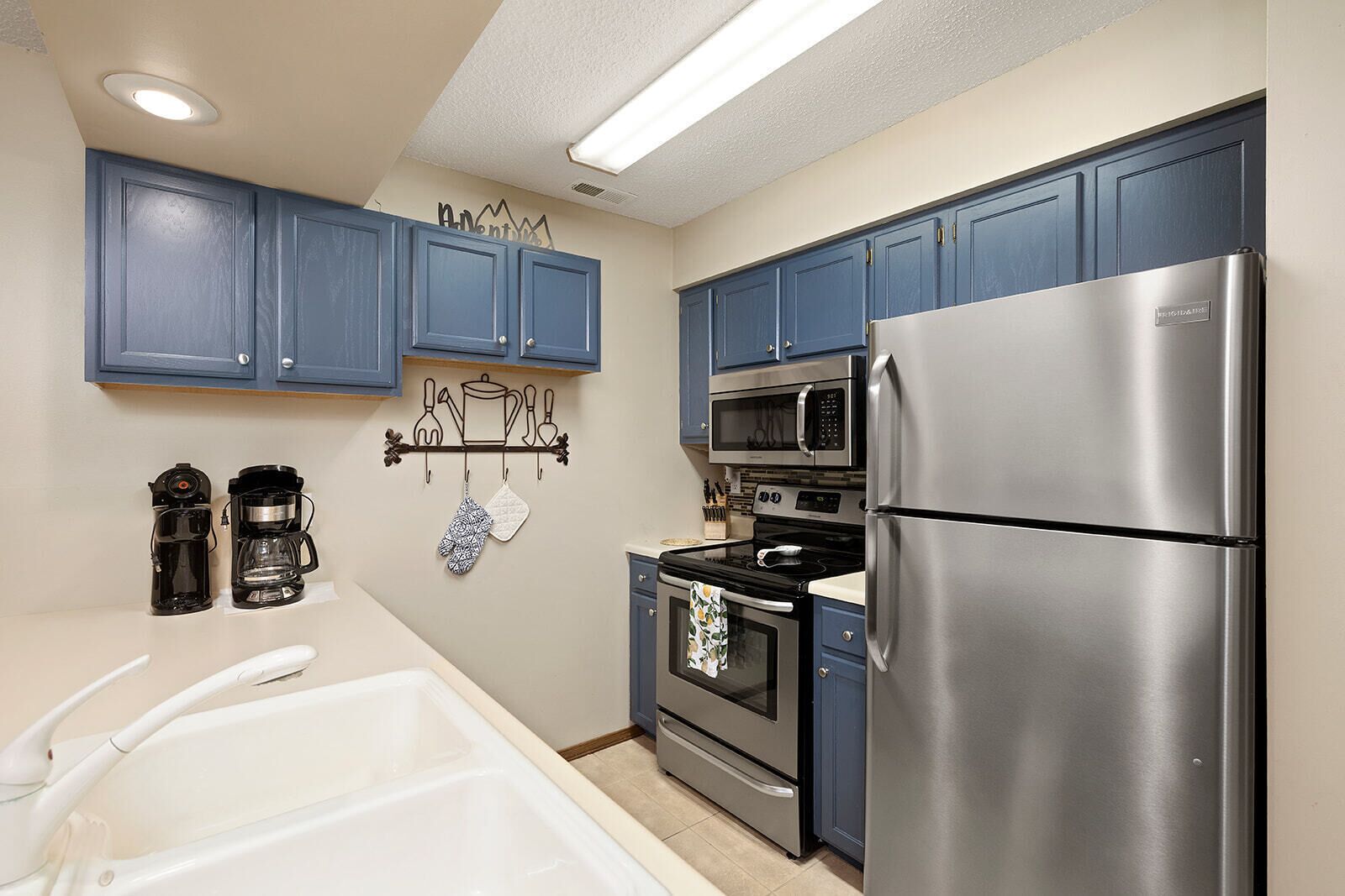 A modern kitchen with blue cabinets, stainless steel appliances, and a coffee maker.