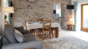 Quarto com paredes de pedra, uma mesa de jantar, cadeiras, um sofá e um relógio de parede grande.