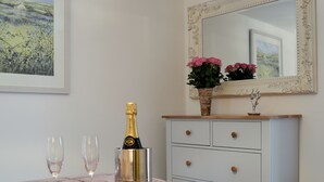 Quarto com uma cama, uma mesinha de cabeceira com uma garrafa de champanhe, dois copos e uma cesta com uma rosa.