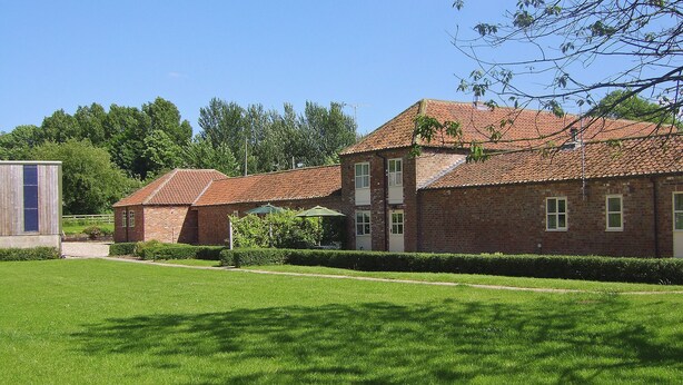A brick building with a tiled roof, surrounded by a well-maintained lawn and trees. - 3 bedroom accommodation in Brigham (Brigham)