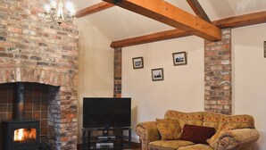 A cozy living room with a brick fireplace, wooden beams, a television, and a patterned sofa. - 3 bedroom accommodation in Brigham (Brigham)