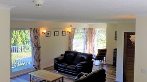 A living room with a sofa, a coffee table, and a view of a balcony. - 4 bedroom accommodation in Lochgoilhead, near Inverary (Lochgoilhead, near Inverary)