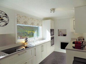 A modern kitchen with white cabinetry, a built-in oven, a microwave, and a window with a view of flowers.