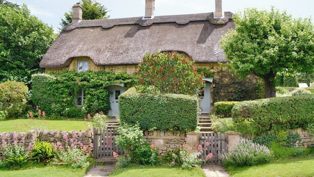 A traditional thatched-roof house with a stone wall and a wooden gate, surrounded by well-maintained gardens. - 2 bedroom accommodation in Westington, Chipping Campden (Westington, Chipping Campden)