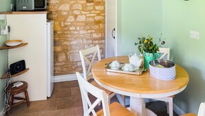 A cozy kitchen with a stone wall, a wooden table set for tea, white chairs, and a microwave on the counter. - 2 bedroom accommodation in Westington, Chipping Campden (Westington, Chipping Campden)