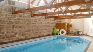 An indoor swimming pool with stone walls, wooden beams, and a tiled floor.