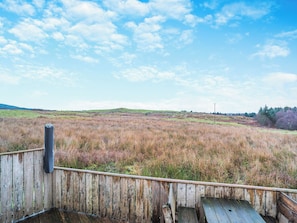 Eine Holzterrasse mit Blick auf ein grünes Feld und einen klaren Himmel.