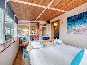 Ein Schlafzimmer mit Holzboden, einem großen Bett, einem Schreibtisch, einem Sessel, einem Fenster und einem Gemälde.