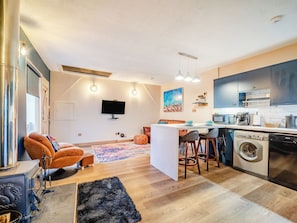 A modern kitchen with a central island, a dining area with a sofa, and a living space with a TV. - 1 bedroom accommodation in Bargrennan, near Glentrool (Bargrennan, near Glentrool)