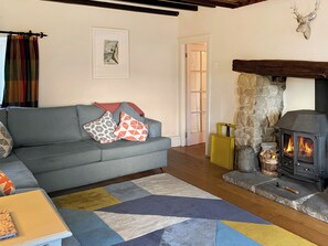 A living room with a grey sofa, colorful cushions, a patterned rug, a fireplace, and a stone wall.