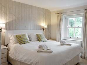 A hotel room with a large bed, two bedside tables, a window with curtains, and a wall with a tree pattern.