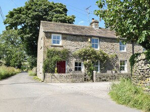 A stone house with a red door, a chimney, and a garden.