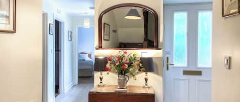 A hallway with a wooden console table, a mirror, and a vase of flowers.